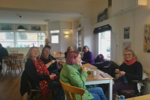 A group of people crocheting at a table at an event at the Baker's Cafe