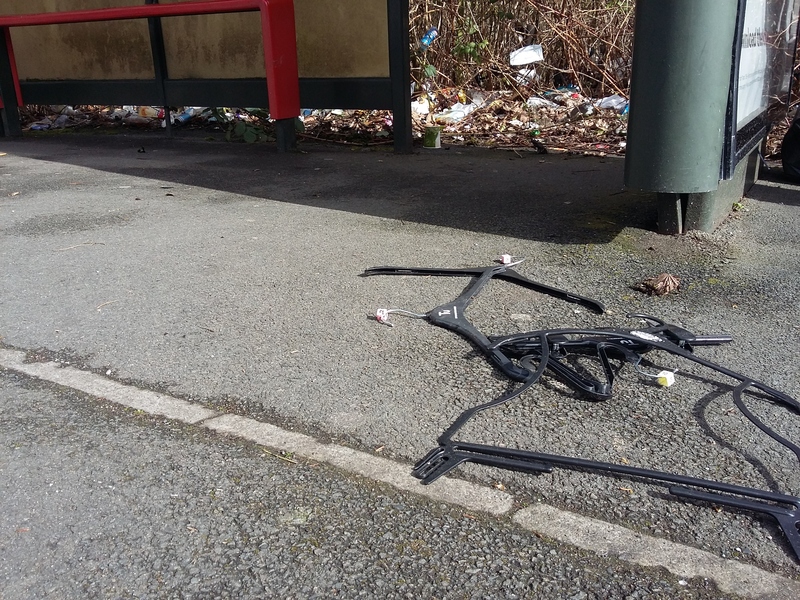 High levels of litter in front and behind a bus stop