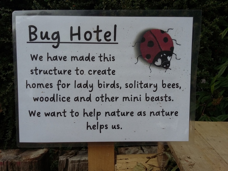 Sign: 'Bug Hotel.  We've made this structure to create homes for ladybirds, solitary bees, woodlice and other mini beasts.  We want to help nature as nature helps us.'