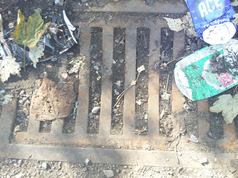 Drain blocked with soil and littered on top with aluminium cans