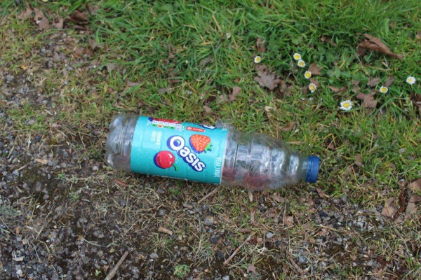 Plastic Oasis bottle littered on an area of soil