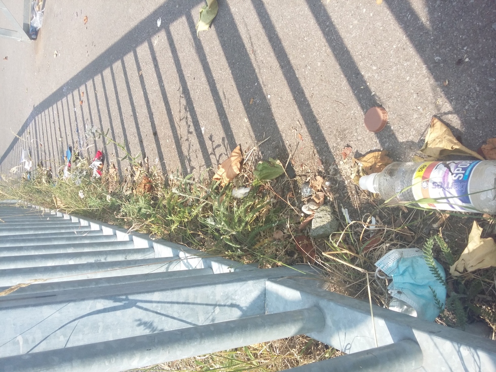 A plastic bottle and other litter by a railing in the skate park