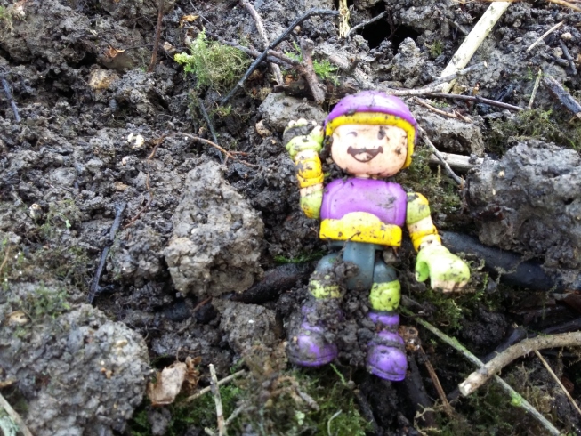 A plastic toy person dug out of the soil