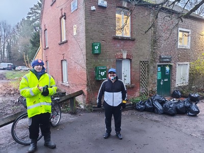 2 litter pickers stand next to a pile of collected rubbish by the Rangers cottage at Coate Water