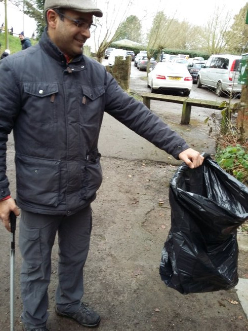 A litter picker uses a stick wrapped around the lip of the bag to hold it open