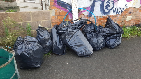 A pile of collected rubbish bags by a graffitied wall