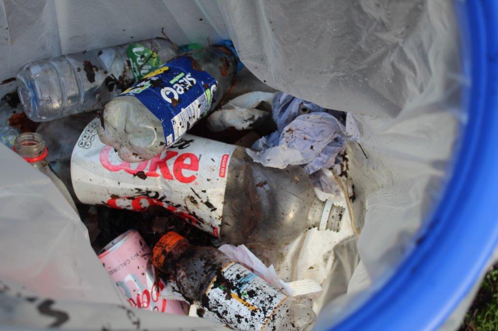 A bag held open with a plastic ring full of cans and plastic bottles