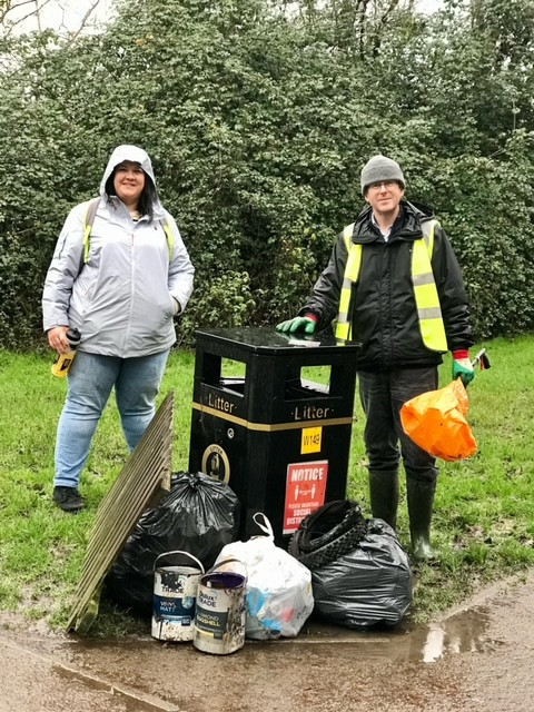 2 litter pickers stand by a bin with assorted rubbish and bags