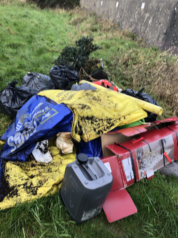 Large items of rubbish including an oil can and plastic bags used for compost piled up on grass