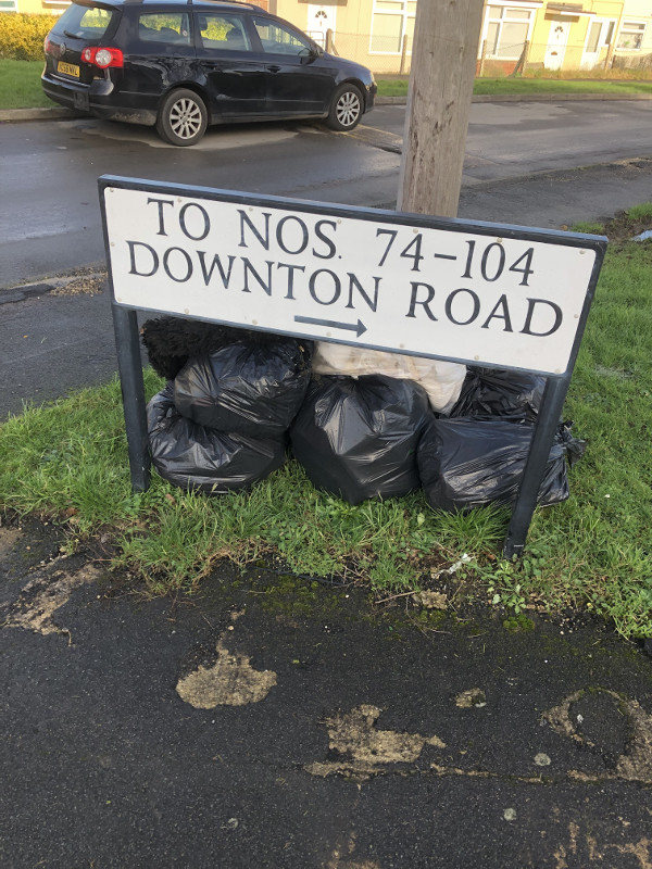 A collection of rubbish bags by the road sign for Downton Road
