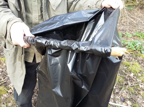 A person holding a plastic bin bag with some of the lip wrapped around a stick