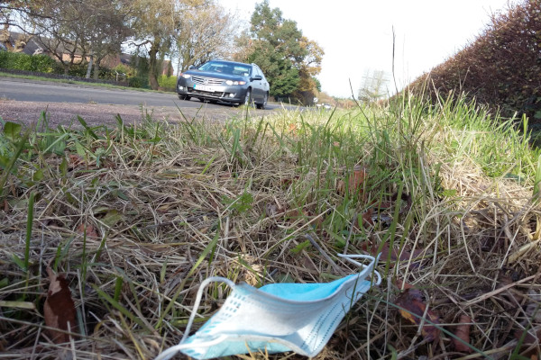 A littered single-use face mask in an area of grass by a road