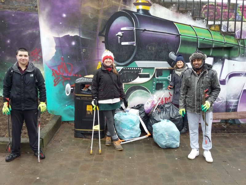 4 litter pickers stand by a bin with their hoard of litter, in front of a graffiti mural