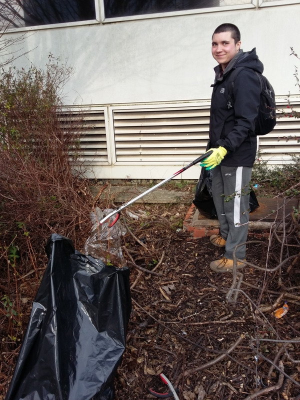 Litter picker stands in front of a building in bushes