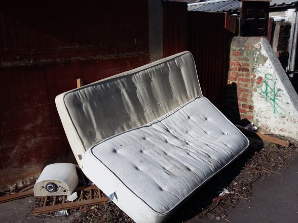 A dumped mattress and other items in an alleyway