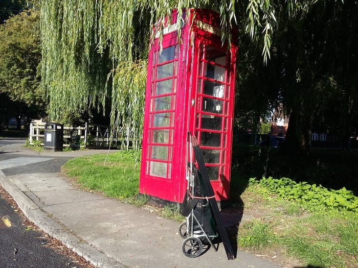PFS stall being transported on a trolley by foot.  By an old fashioned red telephone box.