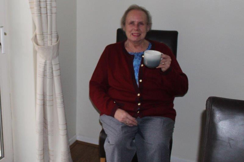 Moya sitting smiling, holding a cup of tea.