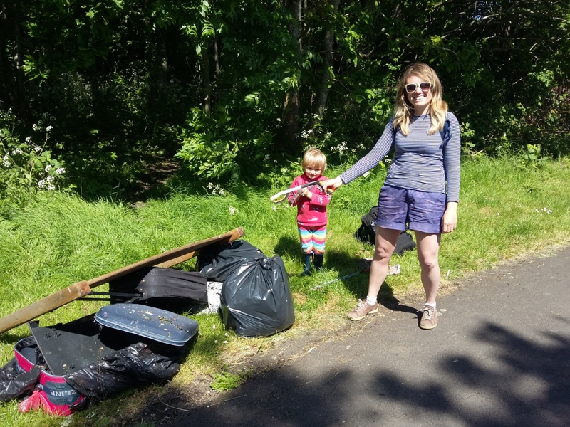 2 litter pickers standing next to fly-tipping removed from woodland