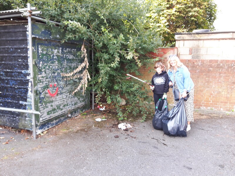 Mother and son hold litter pickers aloft in a car park that they cleaned