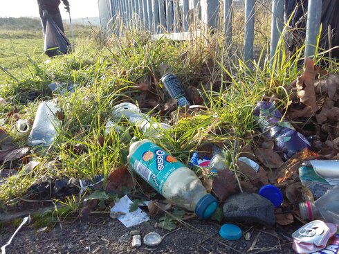 Littered plastic bottles in a grassy area by a railing