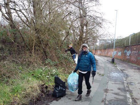 Two litter pickers busy at work cleaning an area of brambles by a path